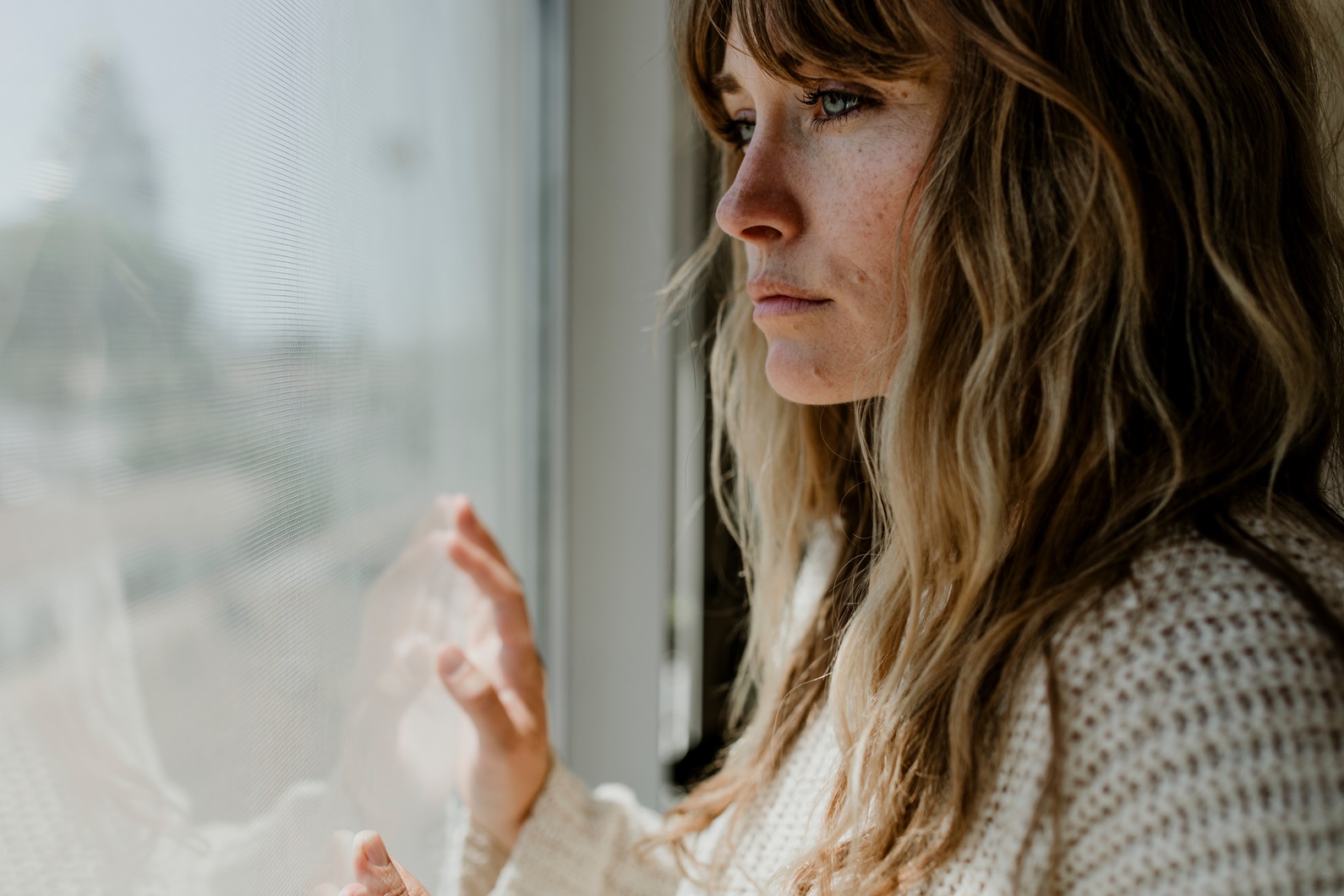 Woman looking out the window in an article by therapist Stefanie Kuhn on how to stop cheating.