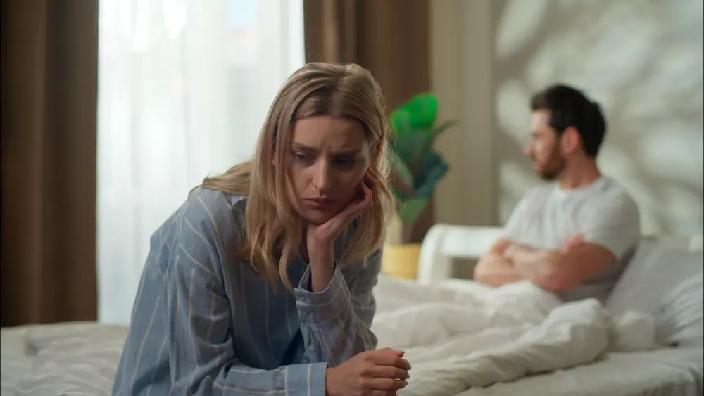 Distressed couple living alone together while sitting apart on a bed after relationship conflict