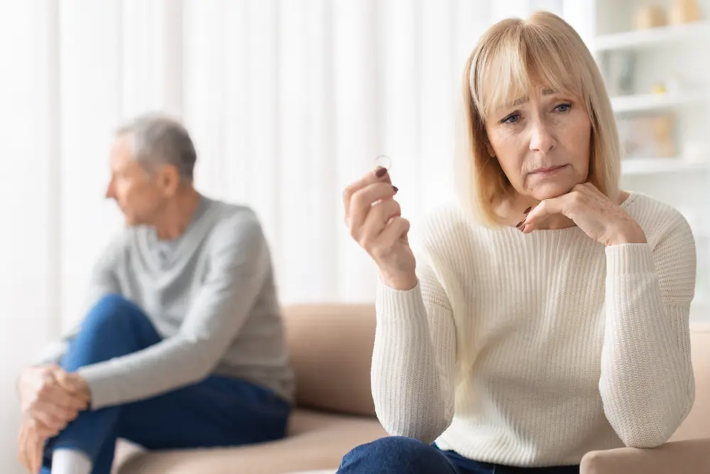 Therapy that works with stefanie kuhn | therapyworks texas Older woman looking thoughtfully at a wedding ring while an older man sits apart in the background suggesting marital separation or divorce